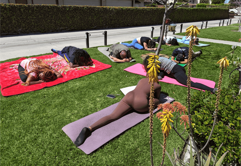 A moment of collective rest during a Magick and Mimosas wellness event, where nine participants are folded in a yoga pose, grounded, supported by the earth.