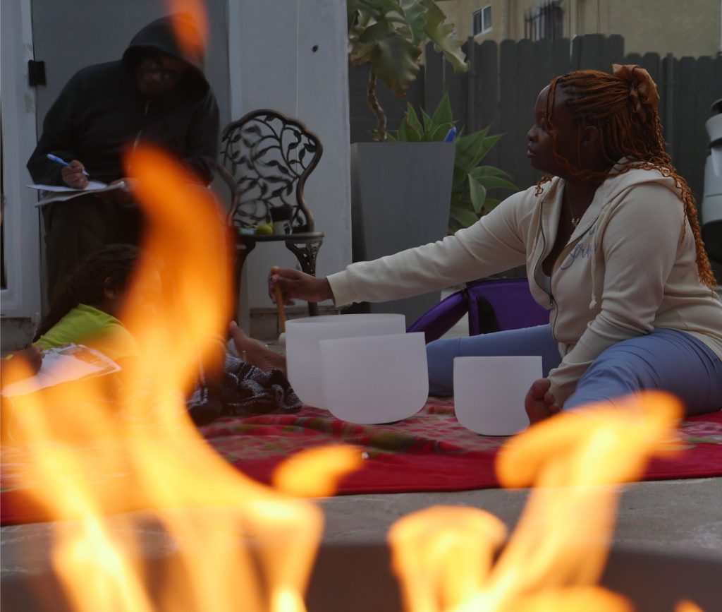 NeNe plays the sound bowls for her mother and children on Winter Solstice while they draw and journal. A fire blazes in the forefront.