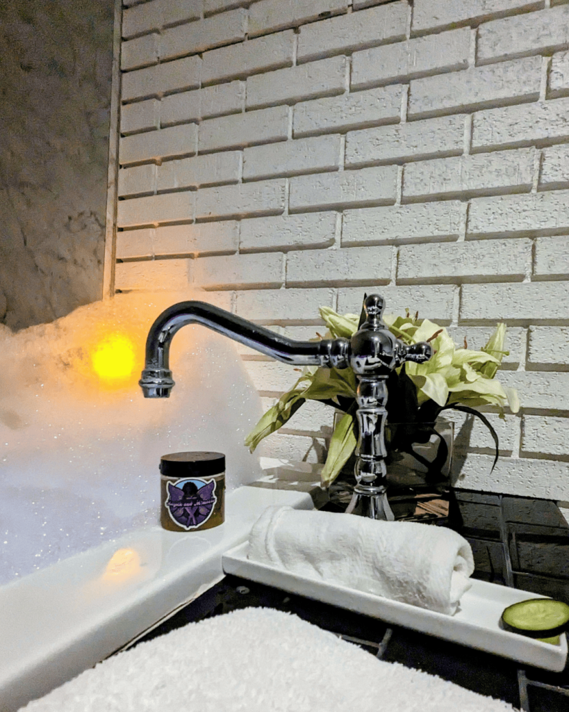Intentional bath ritual featuring spa-style bubble bath, a white tray, a plant, and Magick and Mimosas sugar scrub, representing slow self-care and honoring rest as a practice, especially in winter.