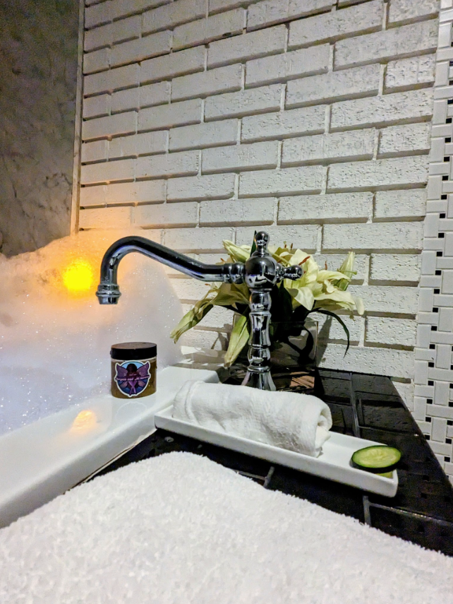 Intentional bath ritual featuring spa-style bubble bath, a white tray, a plant, and Magick and Mimosas sugar scrub, representing slow self-care and honoring rest as a practice.
