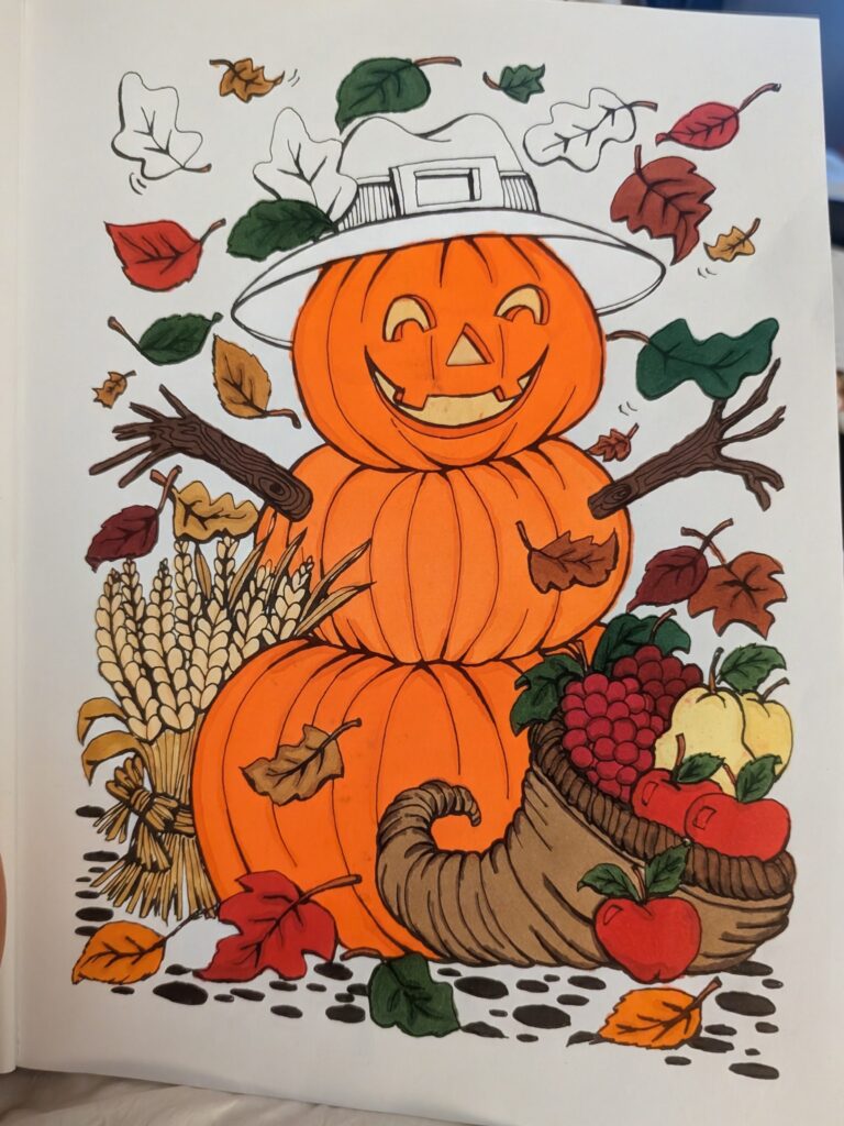 Pictured is a fall themed page of a coloring book that NeNe brought to life with alcohol markers. There are 3 pumpkins stacked on top of each other, with the top pumpkin having a jack o lantern face. Autumn leaves fall in the background and there is a cornucopia with a harvest of fruit in the front. The image is about 90% colored, with the rest left intentionally undone.